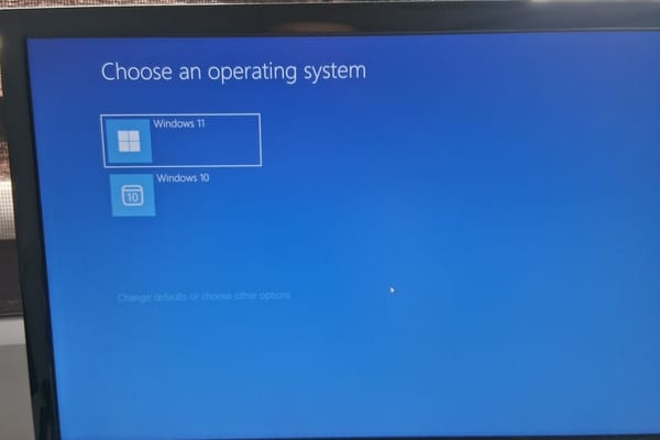 A monitor photographed on a desk, showing a blue screen headed Choose an operating system, listing Windows 11 and Windows 10.